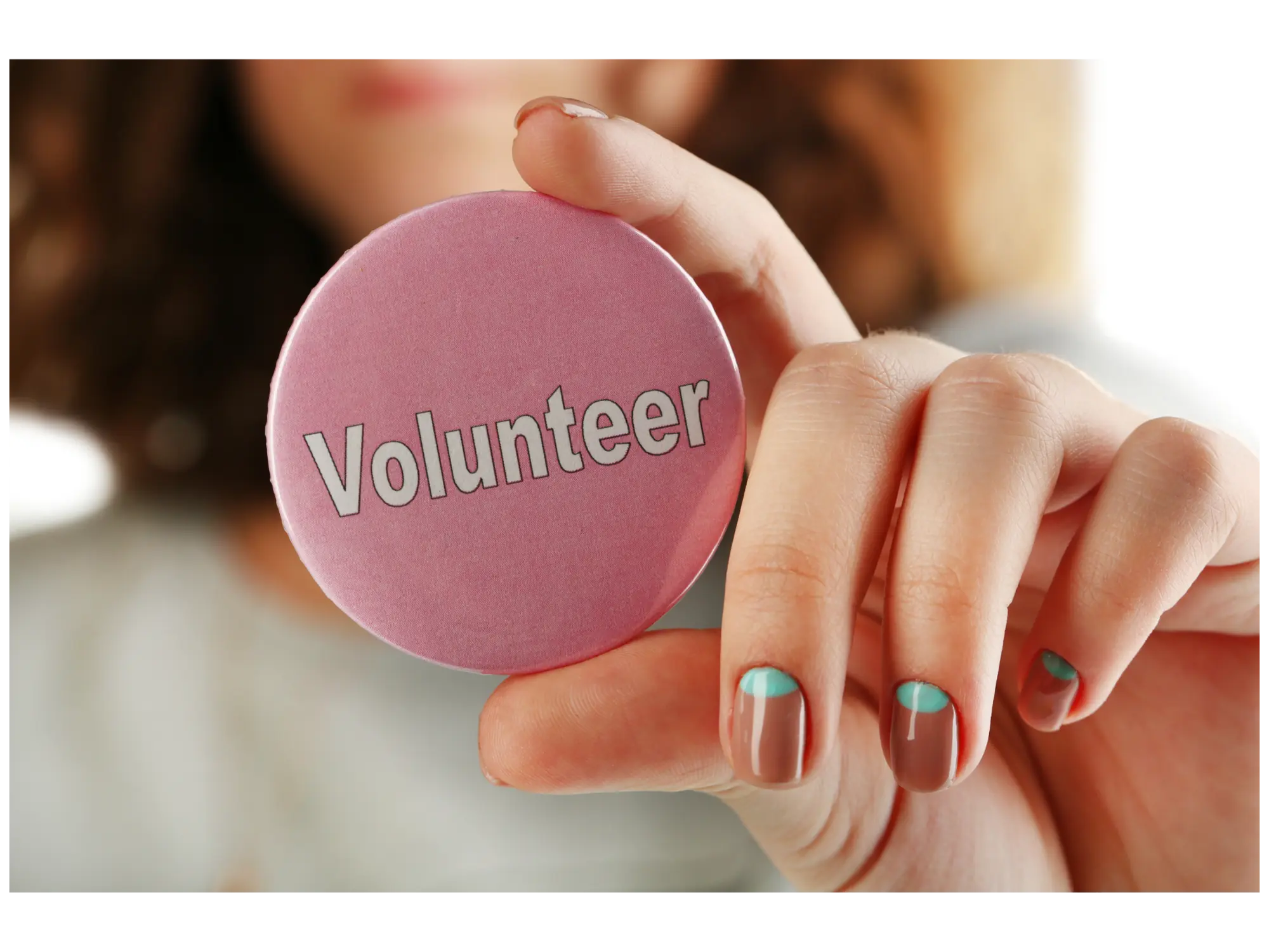 Hand holding a pink Volunteer button