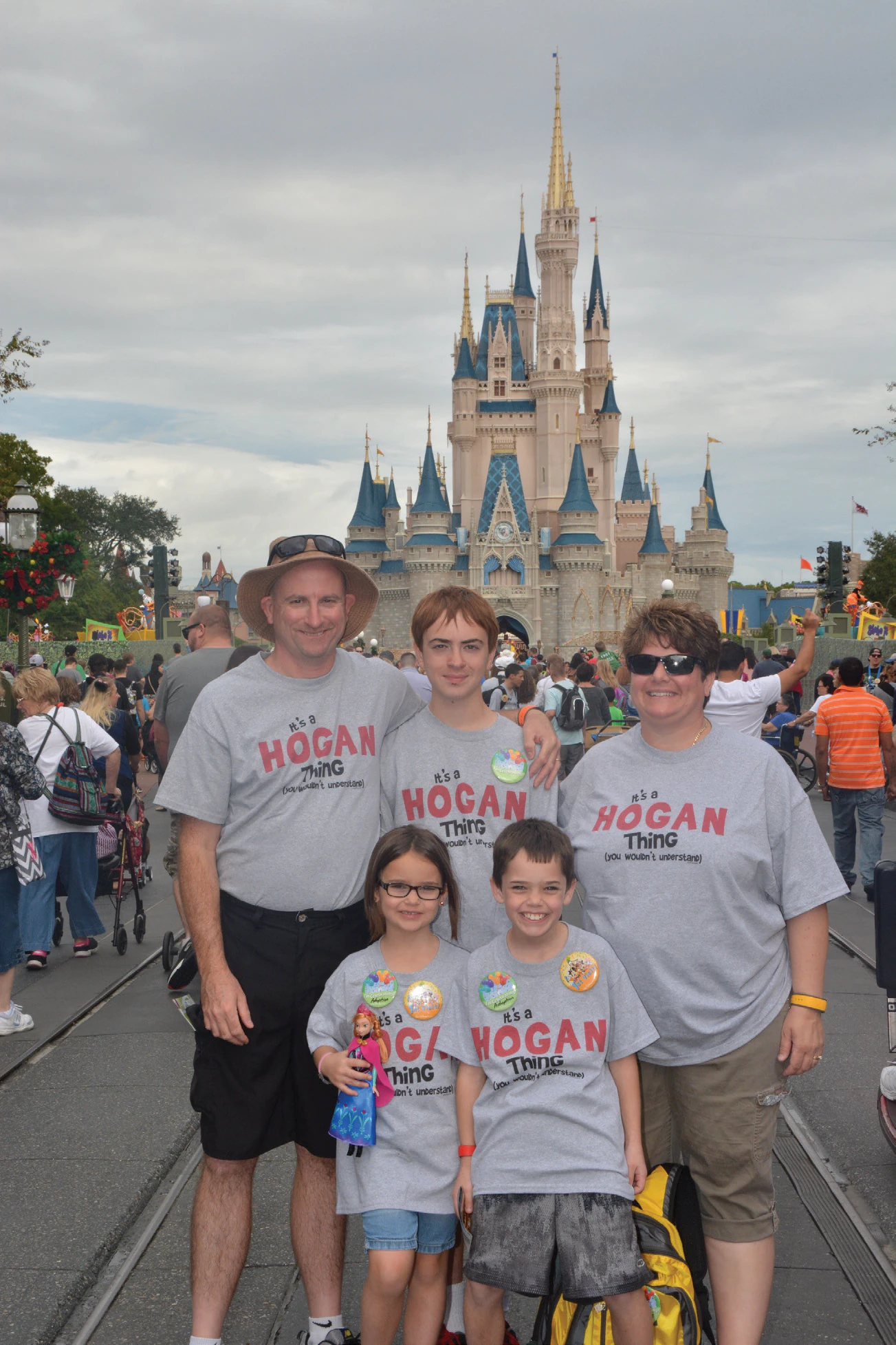Family of five in matching gray Hogan family shirts posing in front of Cinderella Castle at Disney World on an overcast day.