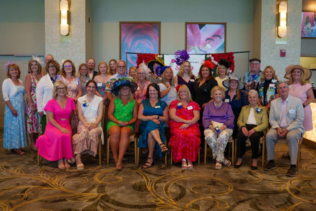 Group of attendees in colorful spring attire and Derby-style hats posing at the 20th Anniversary Swing Into Spring event.